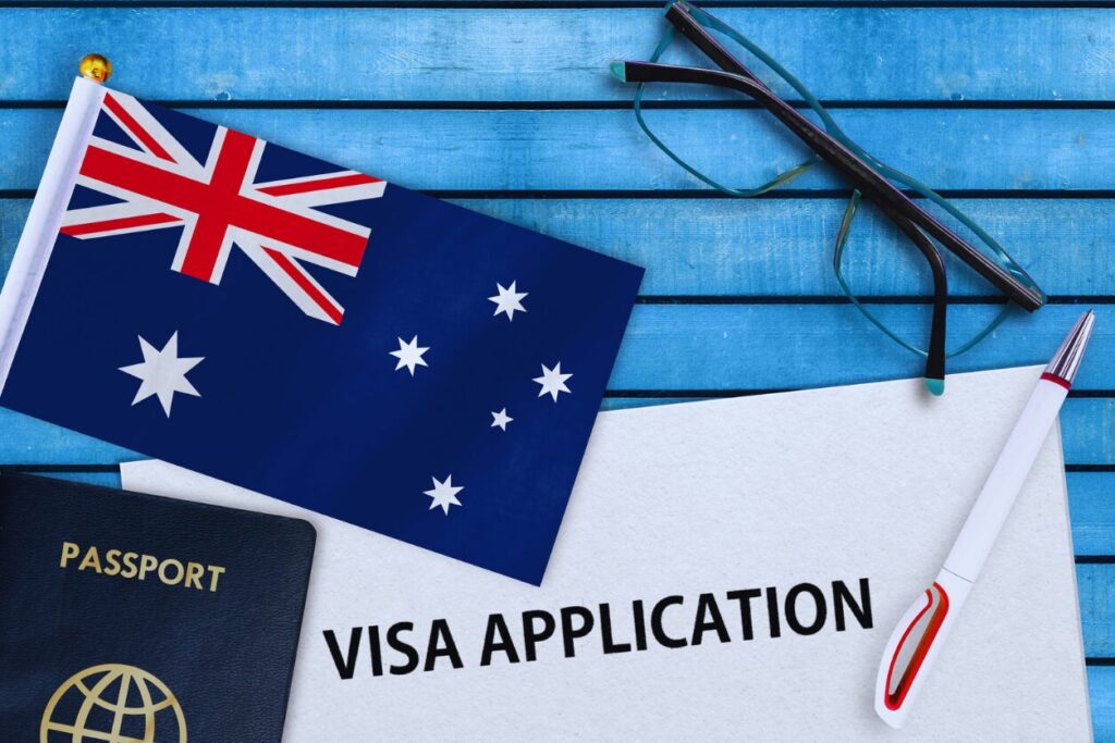 Australian PR Visa application documents with Australian flag, passport, and pen on a blue wooden background.